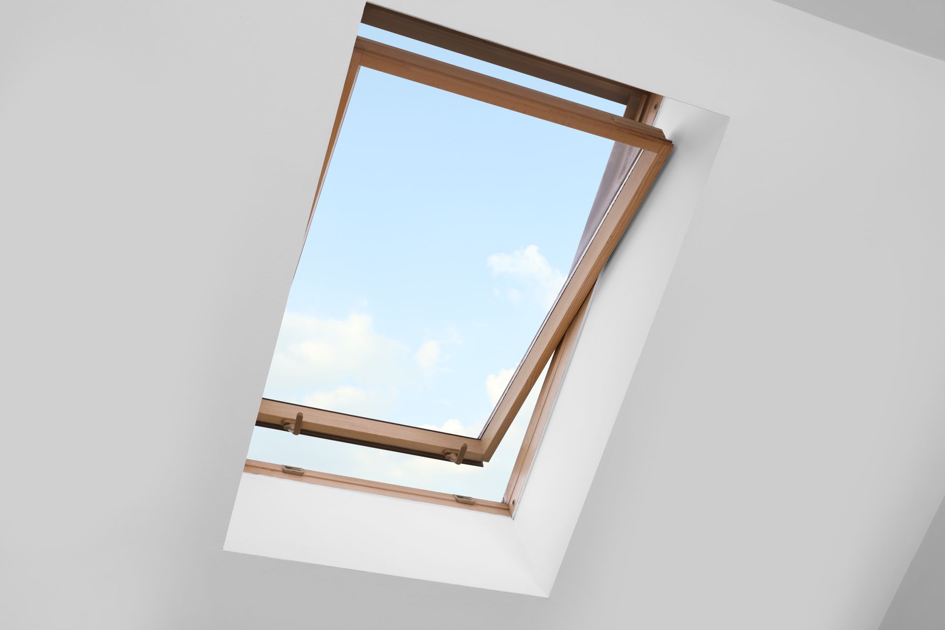 Une fenêtre de toit à cadre en bois ouverte sur un ciel d'un bleu éclatant, intégrée à un plafond blanc uni.