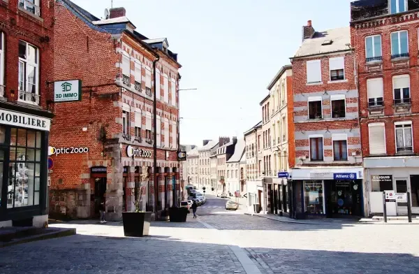 Une rue européenne ensoleillée, bordée de pavés, avec des bâtiments en briques abritant des commerces.