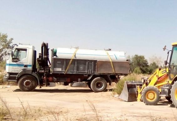 Un camión está siendo remolcado por una excavadora en un campo de tierra.