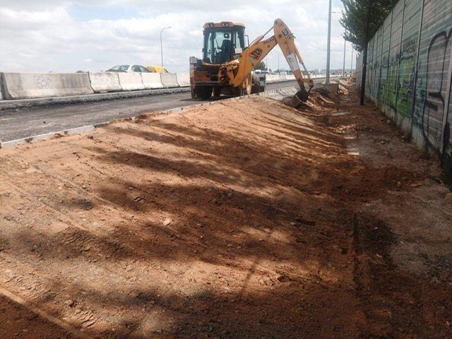 Una excavadora amarilla está cavando un hoyo en la tierra al lado de una carretera.