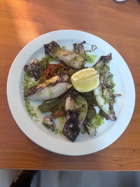 Un plato blanco cubierto con calamares y verduras sobre una mesa de madera.