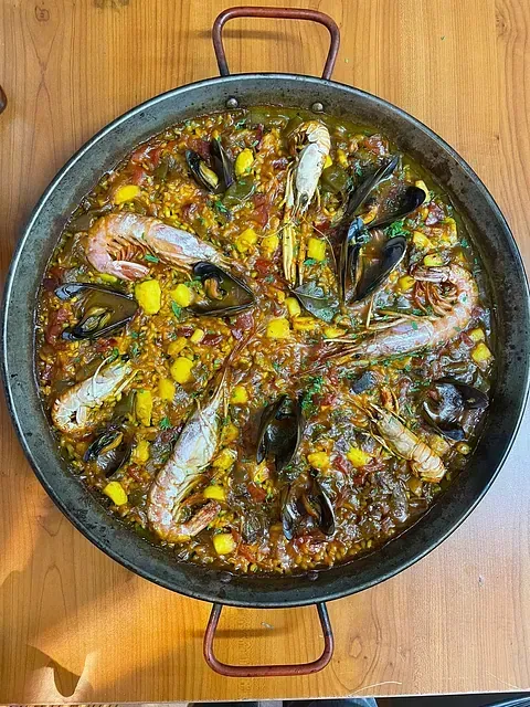 Una sartén de paella con camarones y mejillones sobre una mesa de madera.