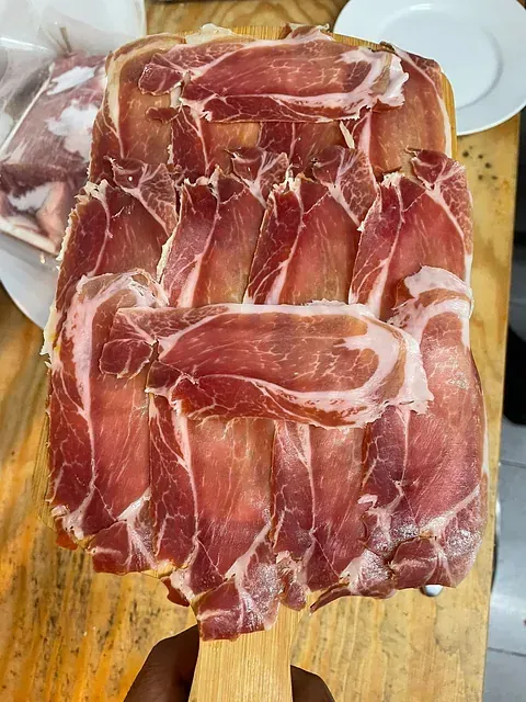 Una persona sostiene una tabla de cortar de madera con rodajas de carne sobre ella.