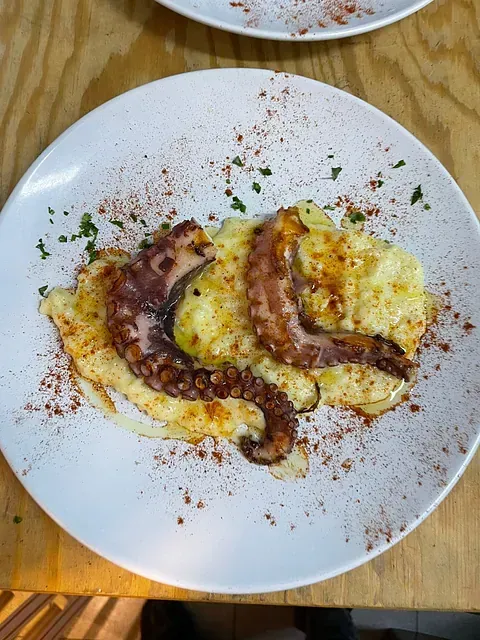 Un plato de comida con un pulpo encima de puré de patatas sobre una mesa de madera.