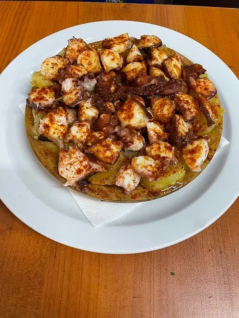 Un plato blanco cubierto con pulpo y patatas sobre una mesa de madera.