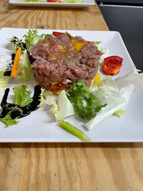 Un plato blanco cubierto con carne y verduras sobre una mesa de madera.