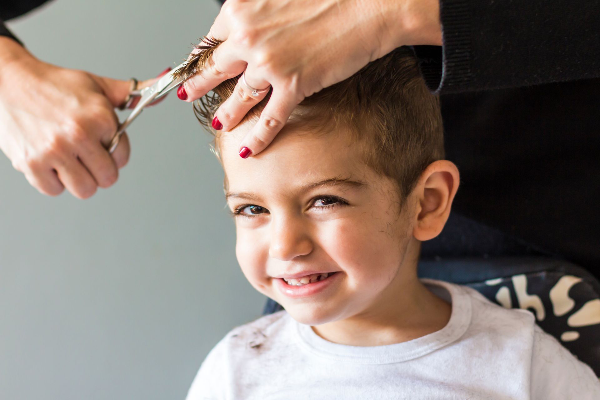 Petit garçon souriant se faisant couper les cheveux avec des ciseaux