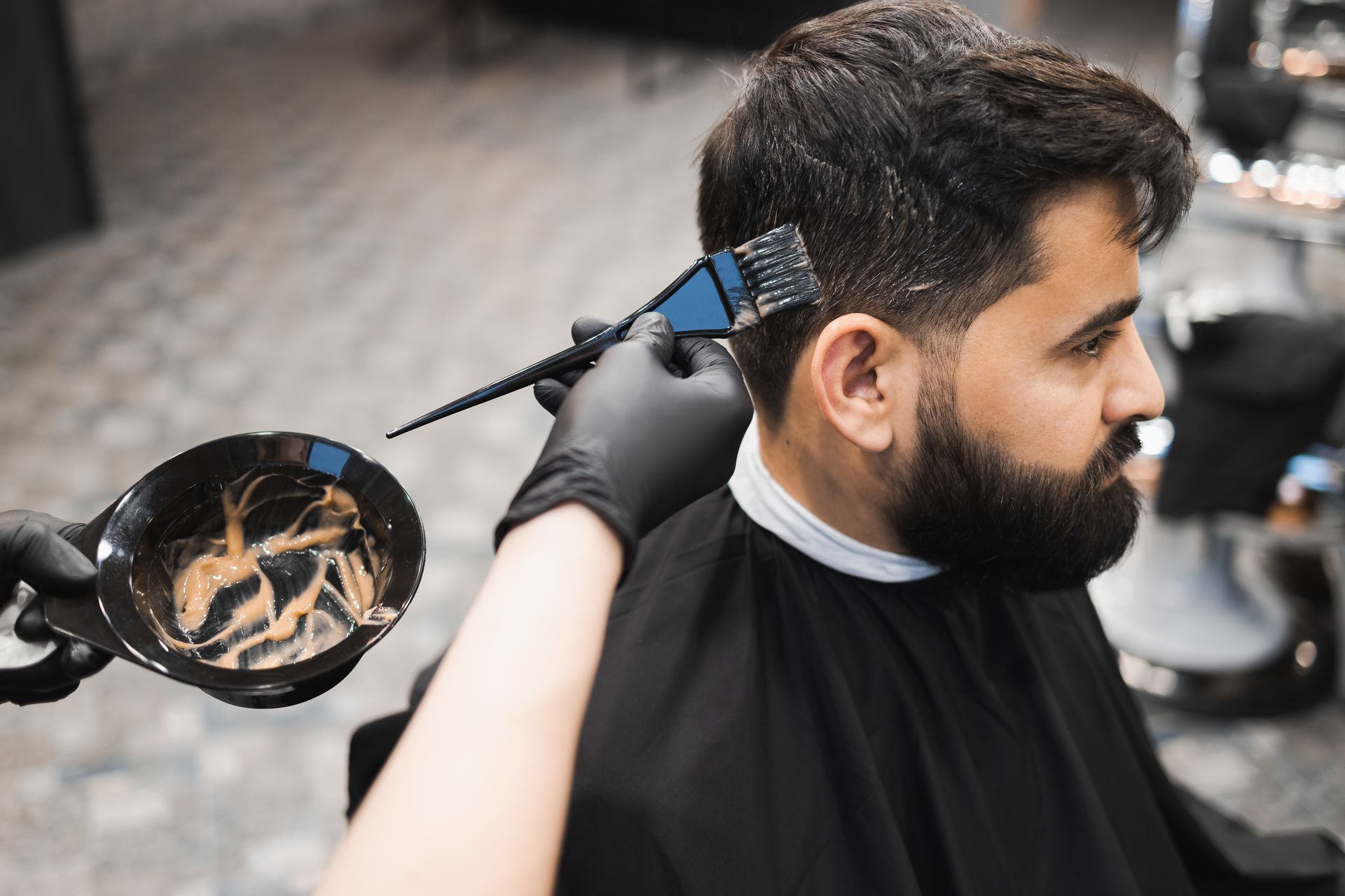 Main gantée tenant un pinceau pour appliquer une coloration sur les cheveux d'un homme