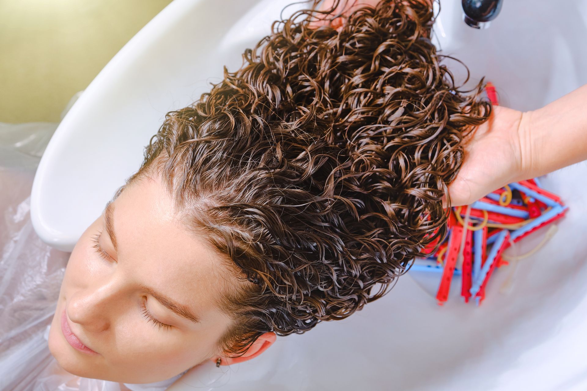 Tête de femme avec chevelure bouclée et bigoudis dans un lavabo 