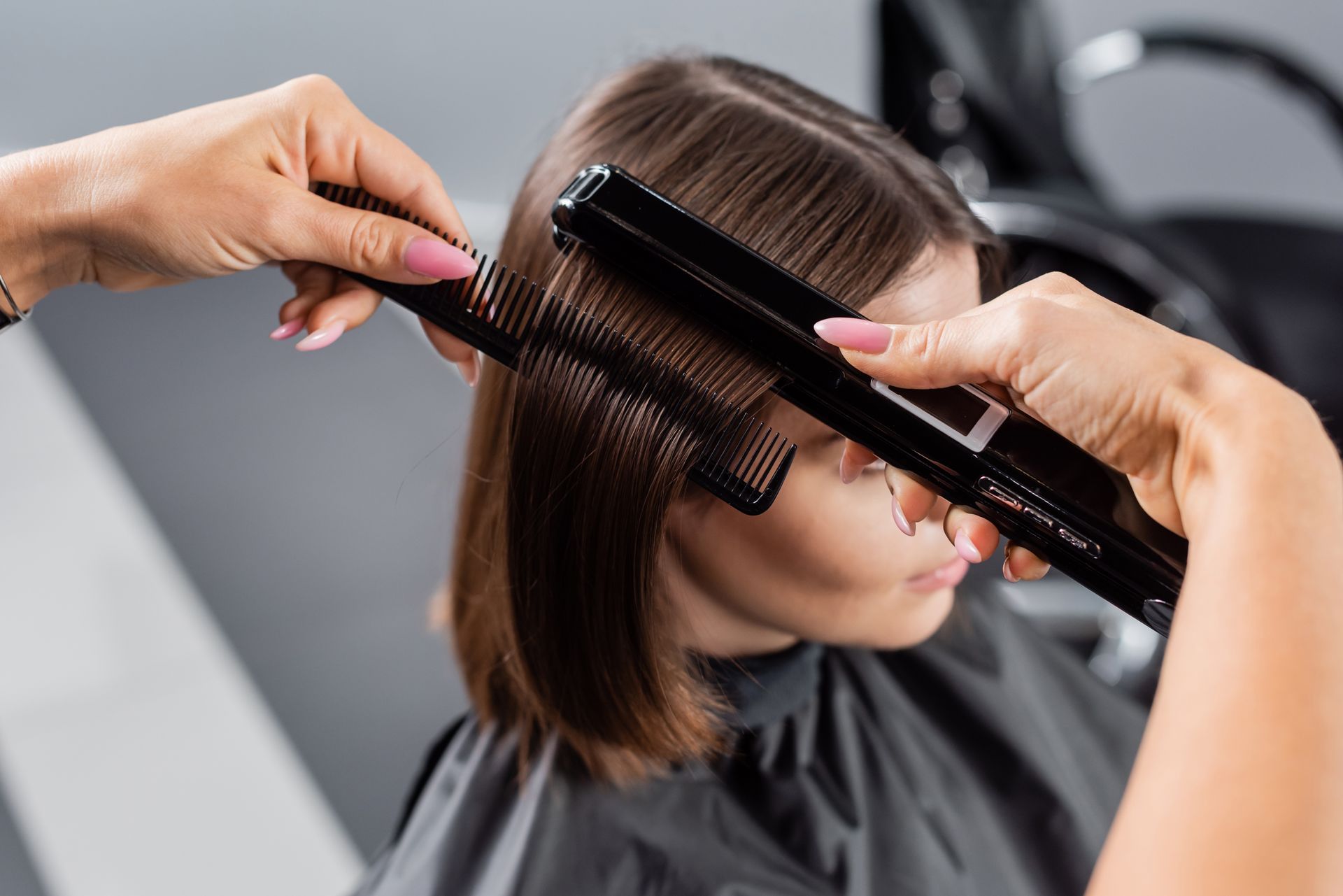 Mains réalisant un lissage avec fer à lisser sur cheveux châtains