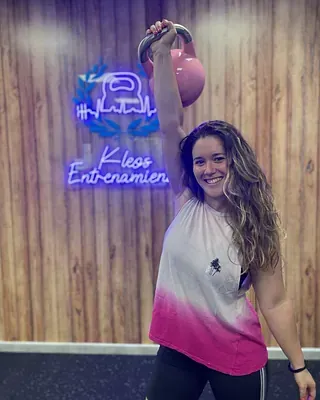 Una mujer sostiene una pesa rusa sobre su cabeza en un gimnasio.