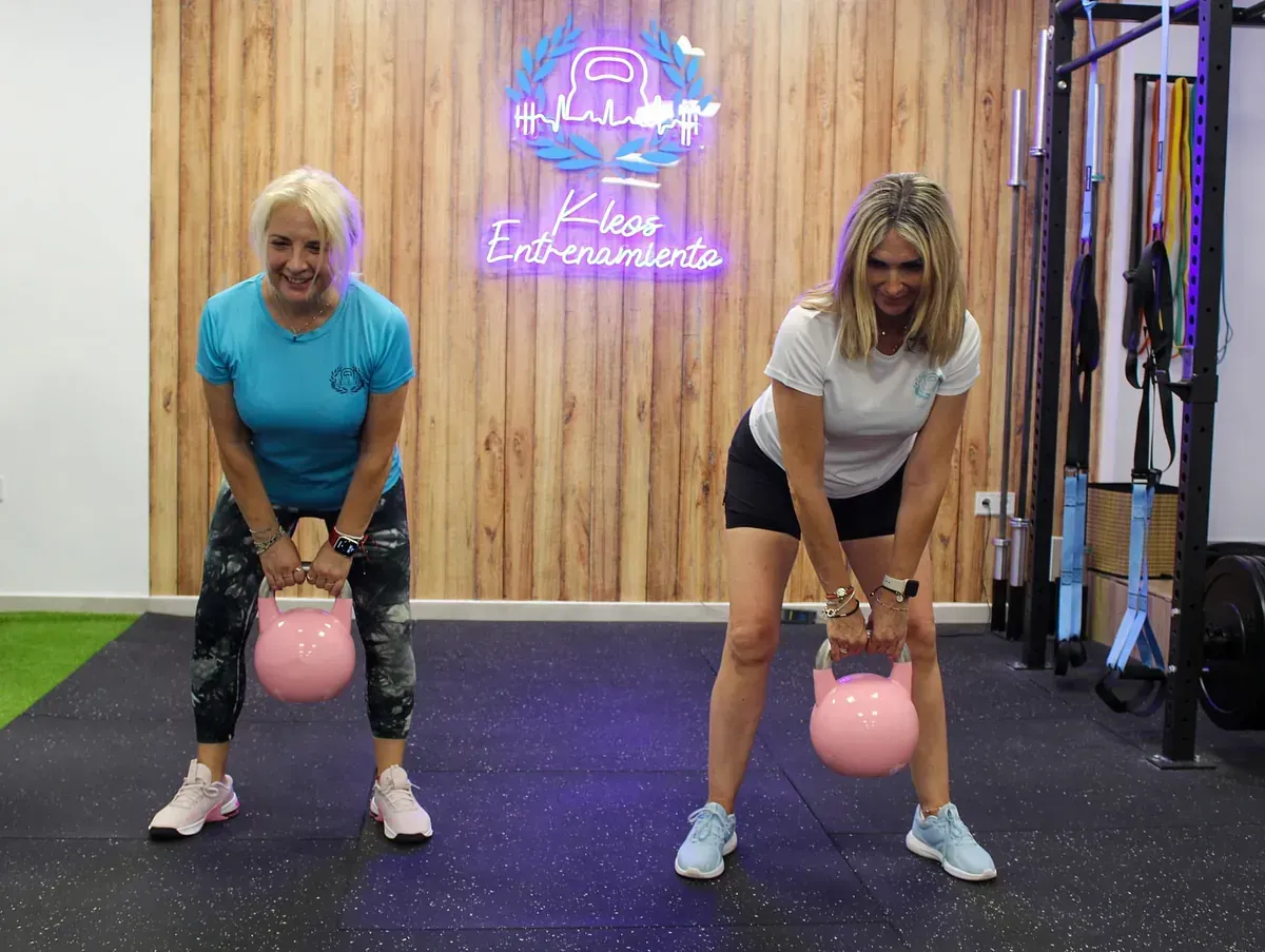 Dos mujeres están paradas una al lado de la otra en un gimnasio sosteniendo pesas rusas.