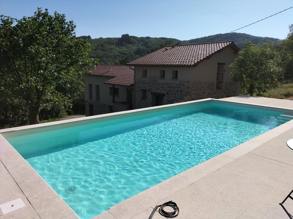 Piscine en béton ensoleillé avec maison rénovée en arrière-plan