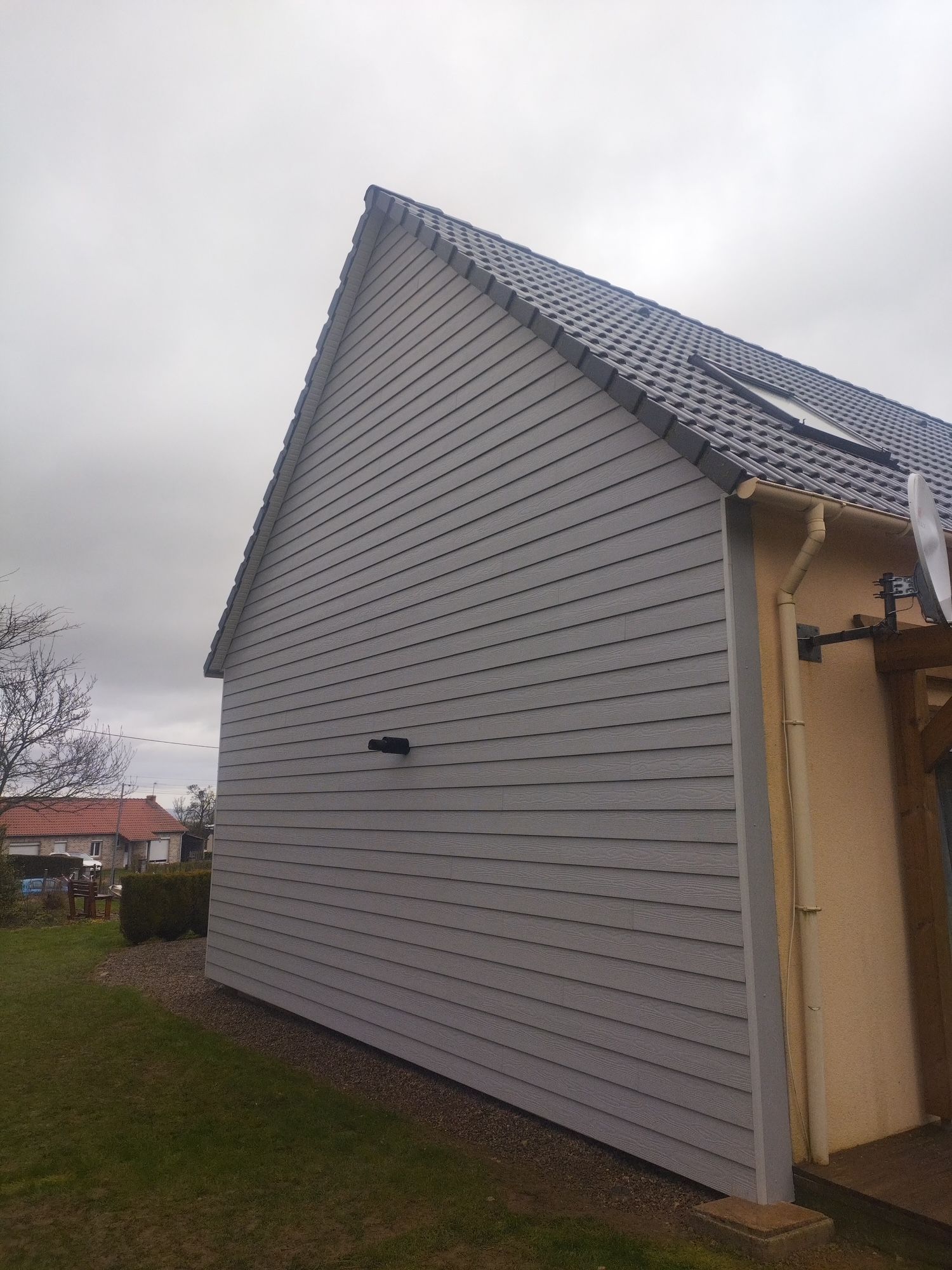 Mur extérieur en bois avec deux fenêtres, stores noirs, bordure de gravier blanc et pelouse verte