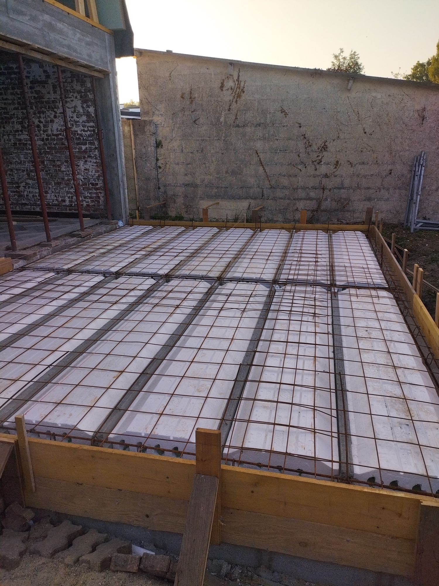 Des mains gantées déposent un bloc de béton sur un mur en construction.