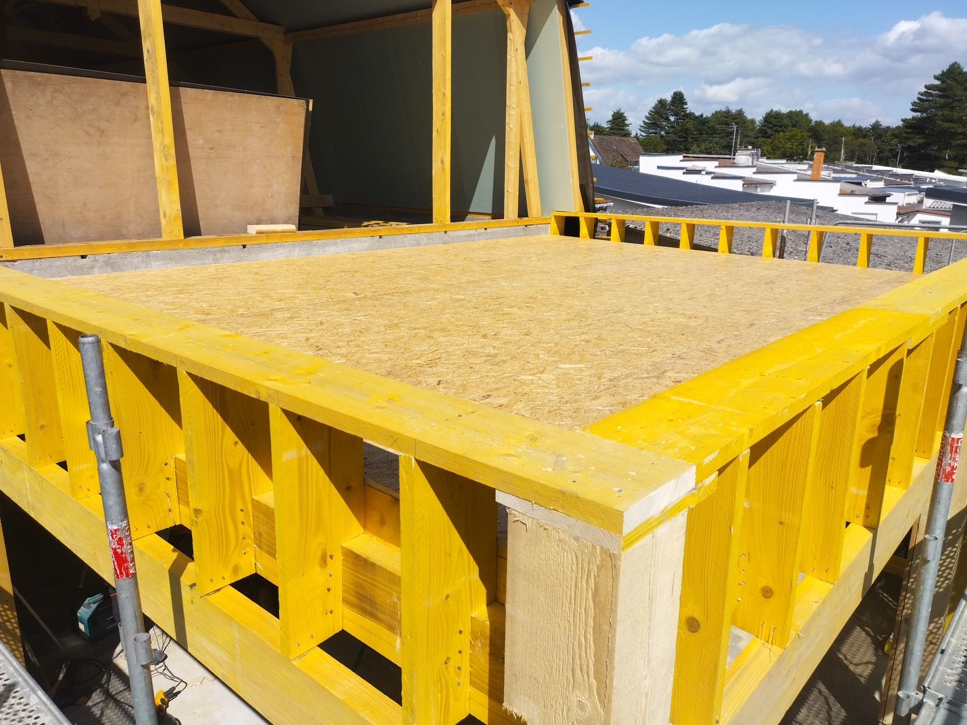 Charpente de toit en bois en construction sur fond de ciel bleu éclatant, le soleil projetant des ombres.
