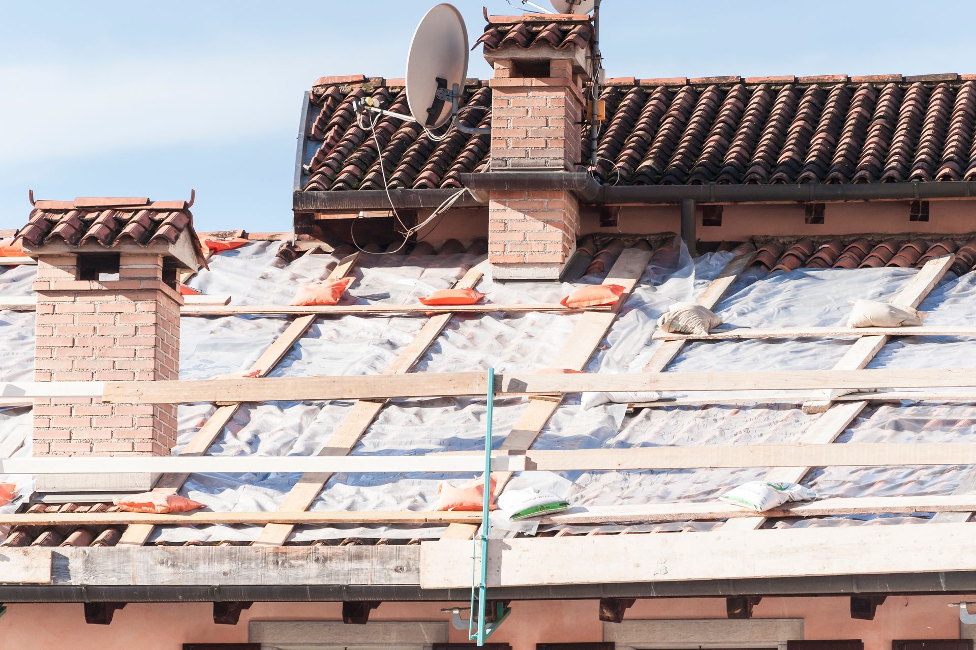 Toiture en réparation avec tôles blanches, poutres en bois et cheminées en briques sous un ciel bleu
