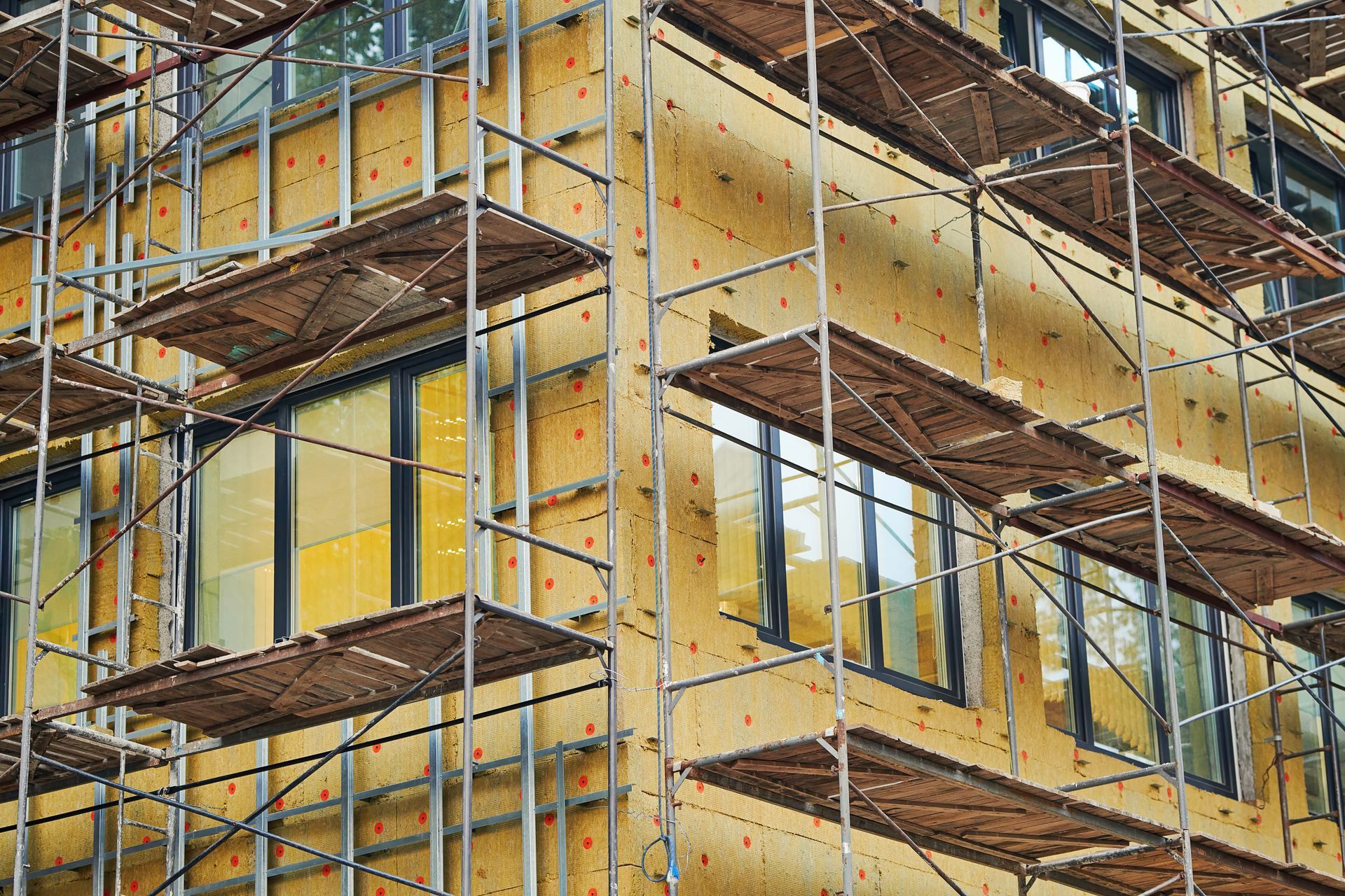Échafaudages autour d'un bâtiment jaune en construction, avec des poutres et des plates-formes métalliques