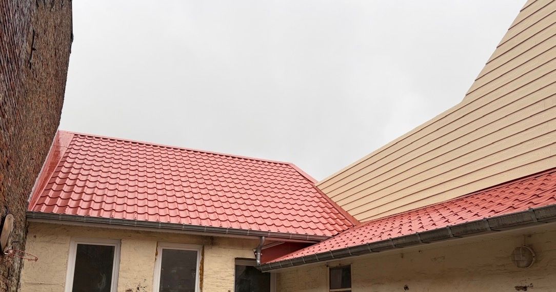 Toit de maison en tuiles rouges avec trois puits de lumière sous un ciel bleu parsemé de nuages