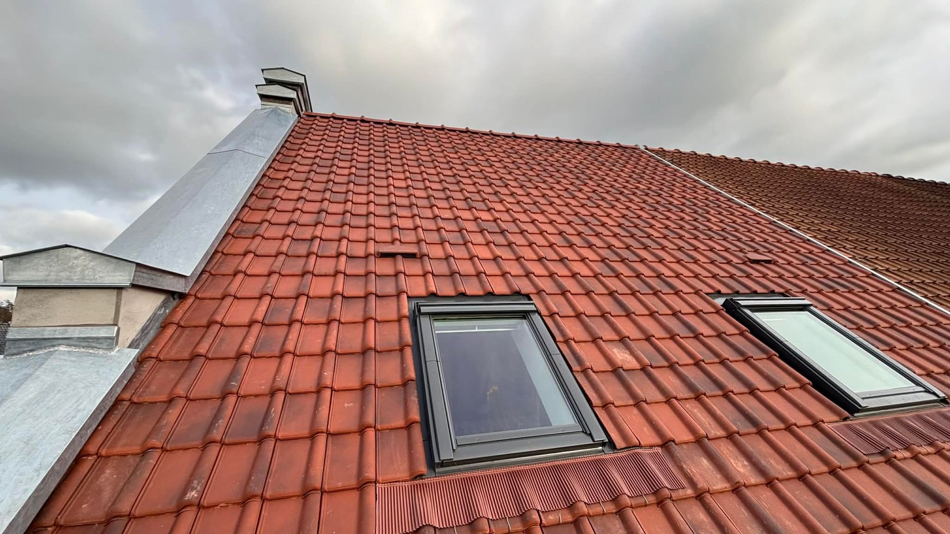 Toit de tuiles rouges avec trois fenêtres de toit sur fond de ciel bleu