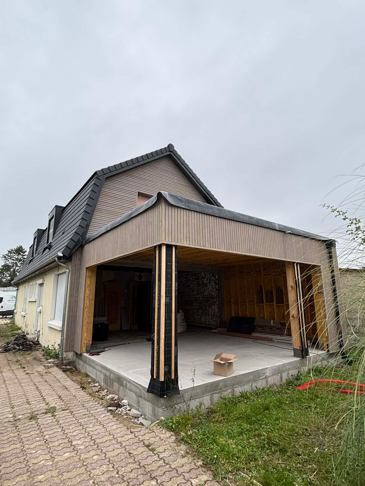 Maison grise à deux étages avec des boiseries blanches et un toit en pente sous un ciel bleu