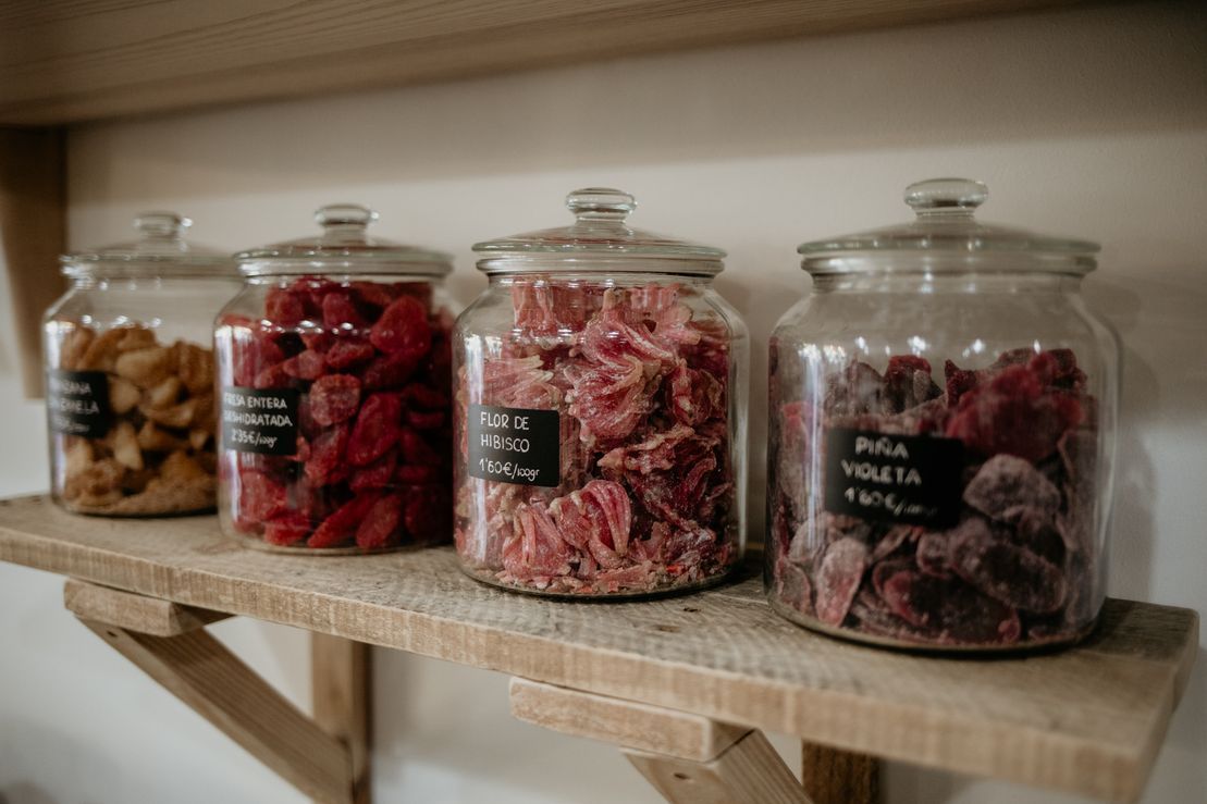 Tres frascos de vidrio llenos de diferentes tipos de dulces están sobre un estante de madera.