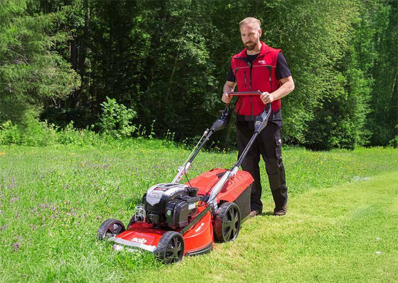 Eine Person mäht mit einem Rasenmäher einen Rasen