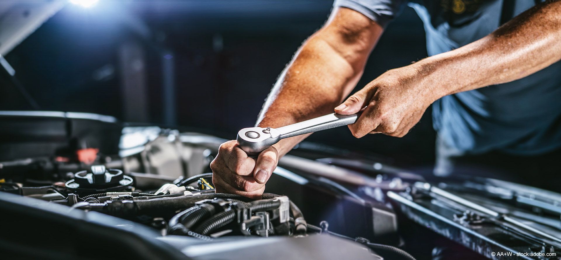 Ein Mechaniker arbeitet unter hellem Licht mit einem Schraubenschlüssel an einem Motor.