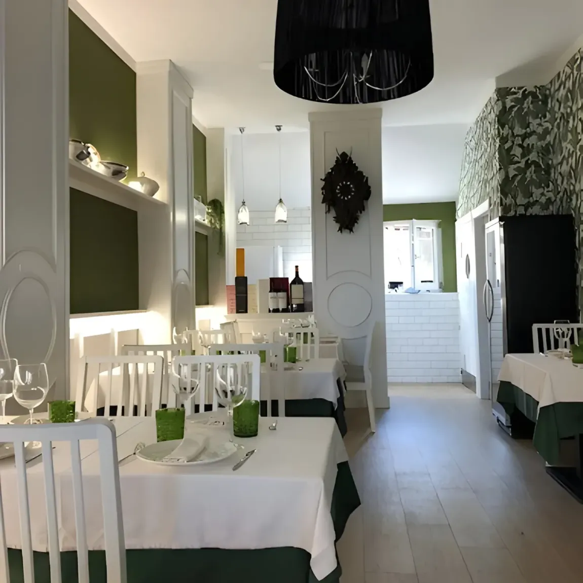 Interior de restaurante con mesas, sillas y paredes blancas; detalles y decoración verdes.