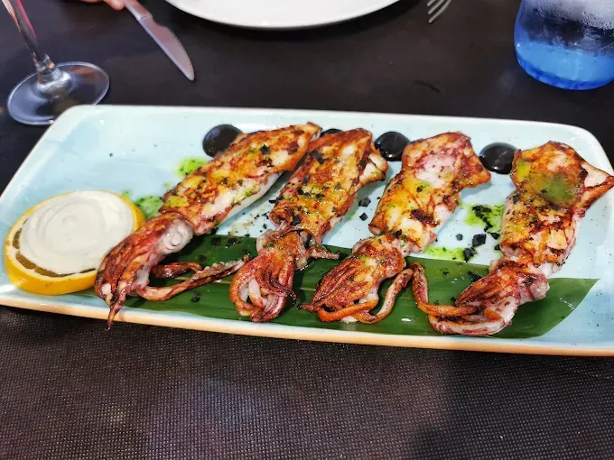 Calamares a la plancha con limón, salsa y aceitunas en plato rectangular.