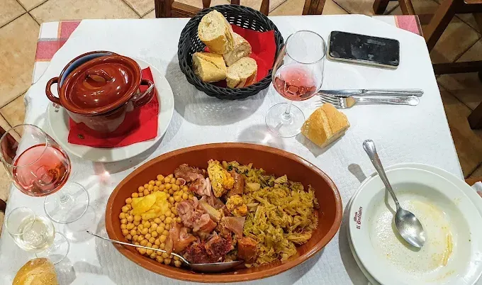 Mesa preparada para la comida: guiso, pan, sopa, copas de vino y un teléfono móvil.
