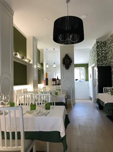 Interior de restaurante Desfilador con mesas y sillas blancas y detalles en verde. Lámpara de araña negra, suelos de madera.