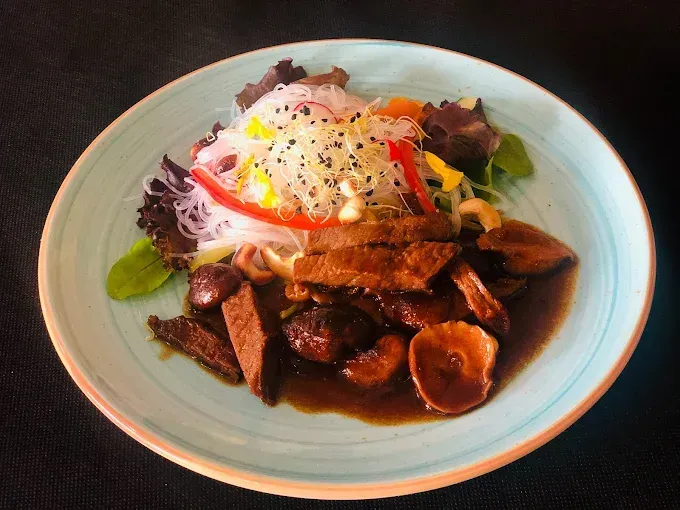 Plato de inspiración asiática en un plato azul claro: carne estofada, champiñones, fideos de cristal y verduras mixtas.