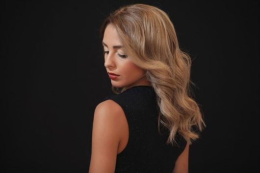 Una mujer con cabello largo y rubio lleva un vestido negro y mira hacia abajo.