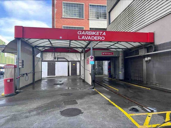 Una instalación de lavado de automóviles al aire libre, con techo rojo, con un área de bahía cubierta y una entrada de túnel.