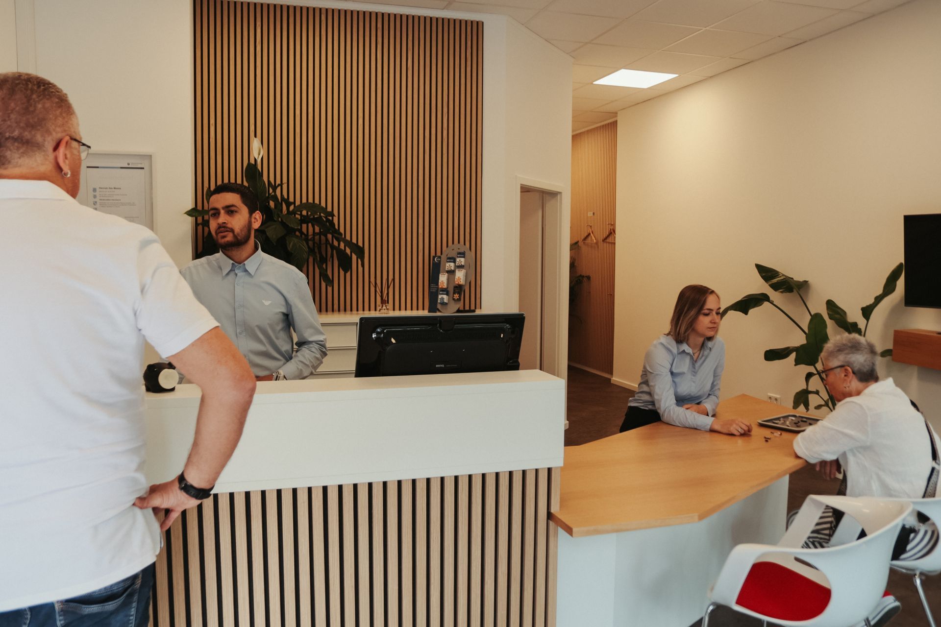 Moderner Büroempfangsbereich mit Leuten, die sich am Empfang unterhalten, und einer Sitzecke in der Nähe.