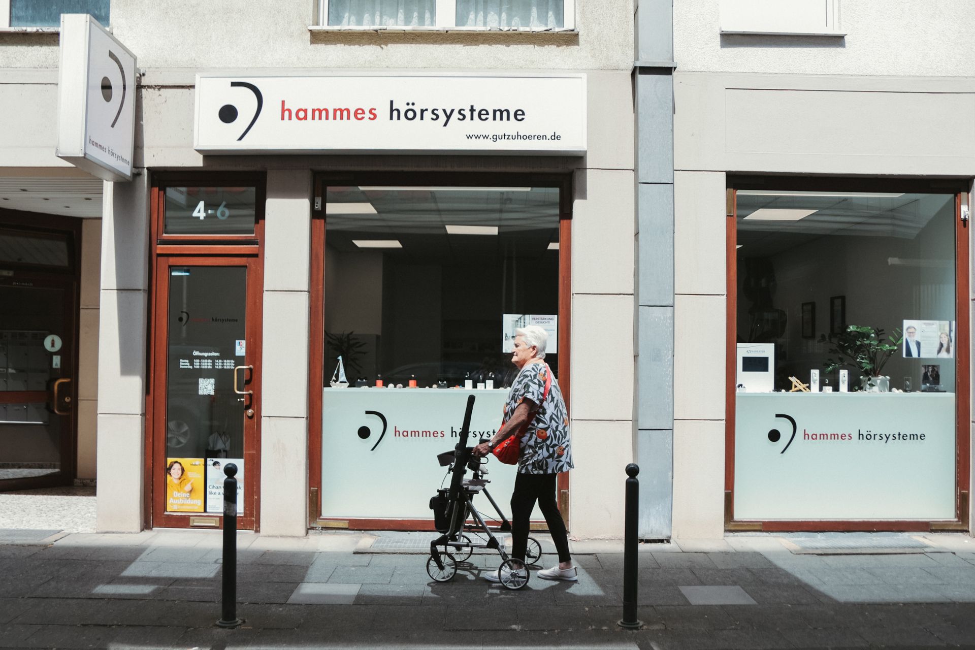 Person, die mit dem Rollator an einem Schaufenster mit weiß-roter Beschilderung vorbeigeht