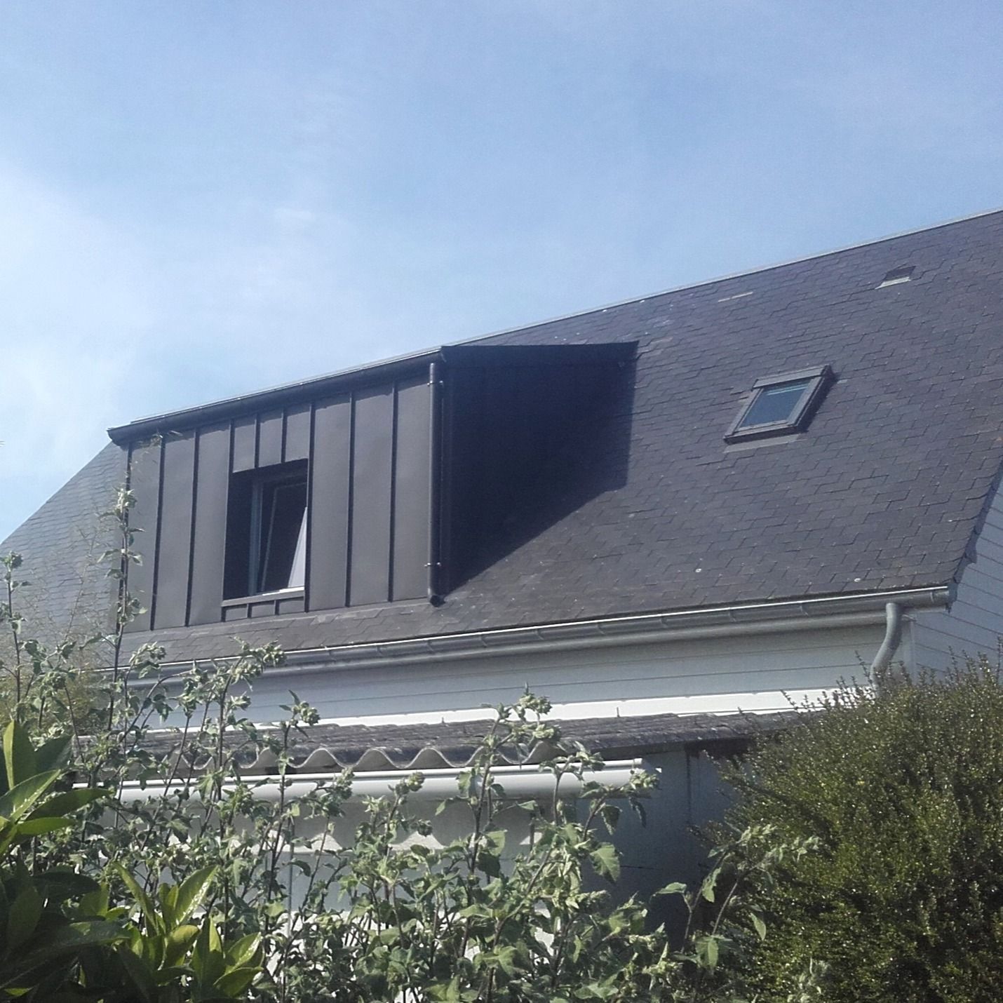 Maison au toit sombre, lucarne et petite fenêtre, par une journée ensoleillée.