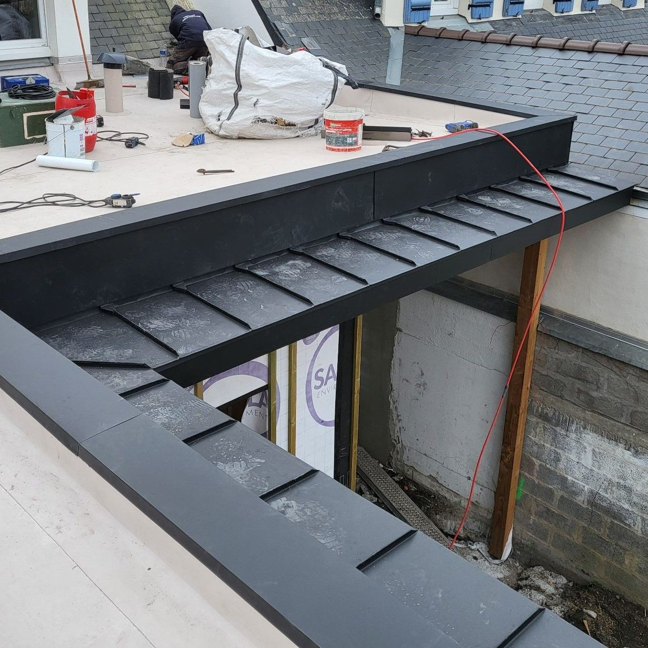 Des ouvriers du bâtiment installent des solins métalliques noirs sur un toit. Vue extérieure, lumière du jour.