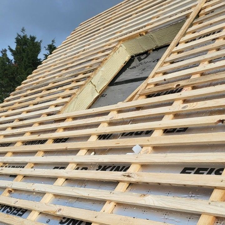 Toit végétalisé avec poutres en bois, cheminée et arbres environnants.