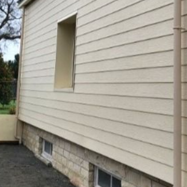 Bardage beige sur un bâtiment avec une fenêtre et une gouttière à côté d'un angle en pierre.