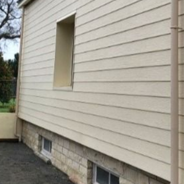 Bardage beige sur un bâtiment avec une fenêtre et une gouttière à côté d'un angle en pierre.