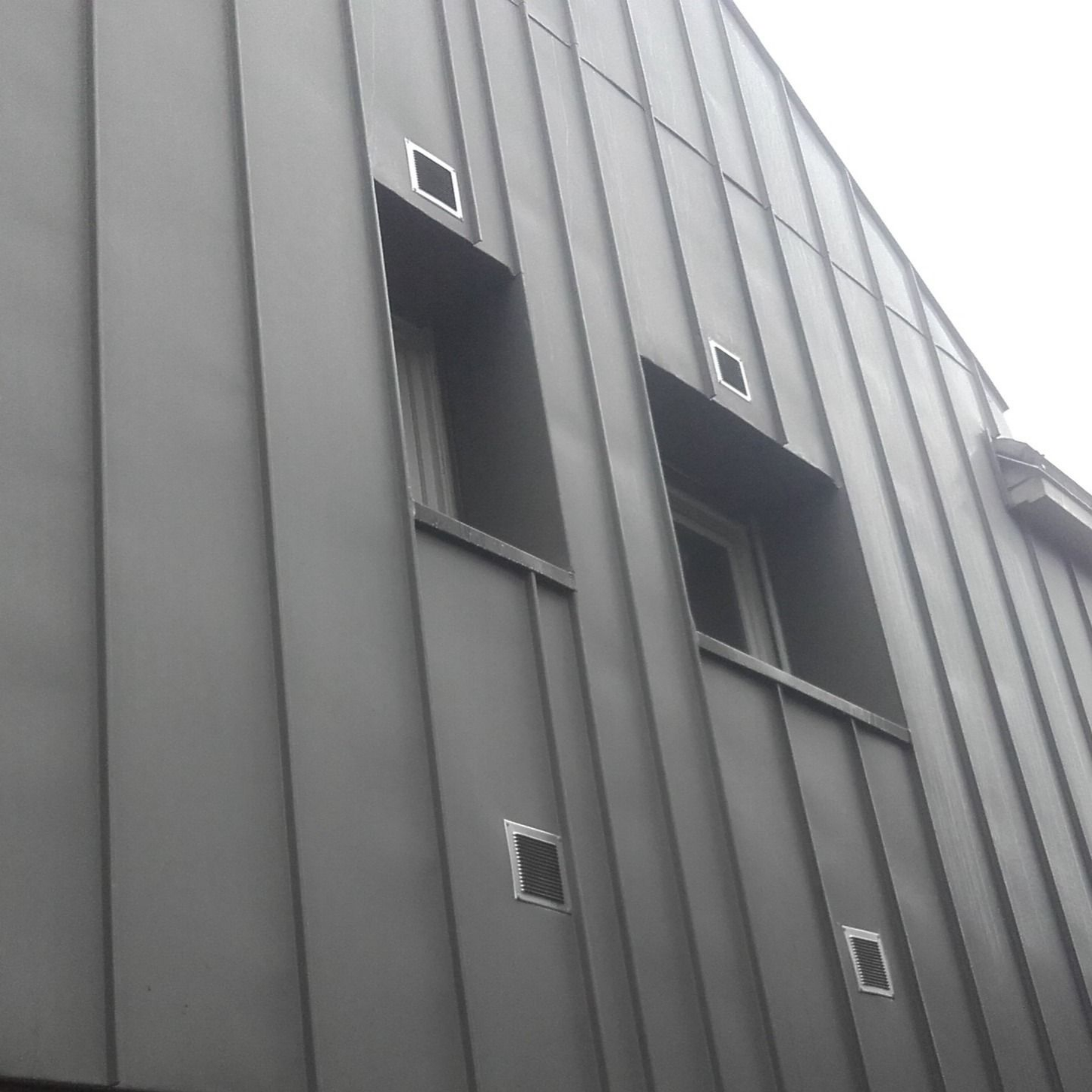 Un bâtiment de deux étages avec une façade de magasin. La boutique présente des touches de vert et de gris, et une enseigne indiquant L'Écrin.