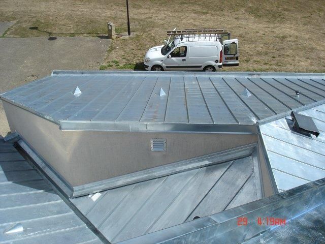 Toit en métal avec une camionnette blanche en arrière-plan, probablement un chantier de construction.