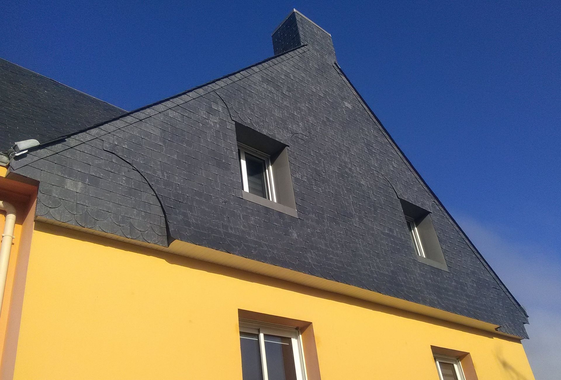 Bâtiment revêtu de métal gris, avec deux fenêtres et quatre aérations carrées. Des branches encadrent le côté.