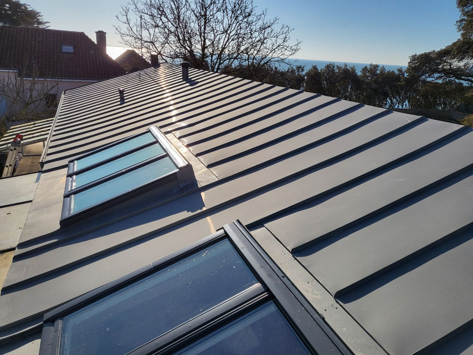 Panneaux solaires installés sur un toit de tuiles sombres, ciel bleu vif en arrière-plan.