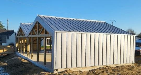 Hangar en construction, à structure métallique apparente et toit en tôle ondulée, se détachant sur un ciel bleu.