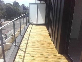 Balcon en bois avec rambarde en métal, panneaux de verre et revêtement extérieur sombre.