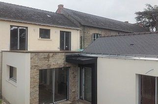 Extérieur d'un bâtiment rénové aux murs clairs, en pierre, avec des fenêtres sombres et un toit gris.
