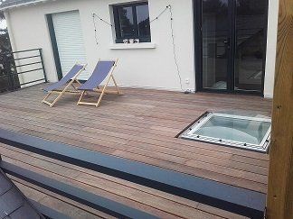Terrasse en bois avec deux chaises longues, puits de lumière et accès à une maison.